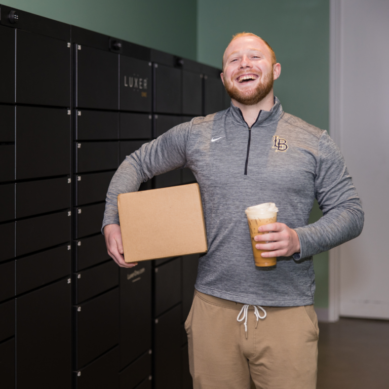 Resident holding package and coffee smiling in front of Luxer One smart package lockers