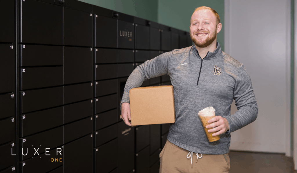 University student happily holding package in front of black, Luxer One, smart package lockers