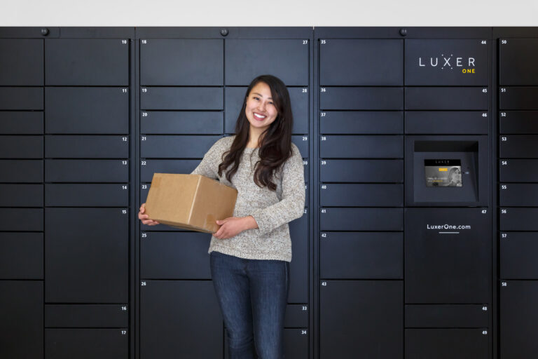 Happy resident with package next to the Luxer One smart package lockers at their apartment community